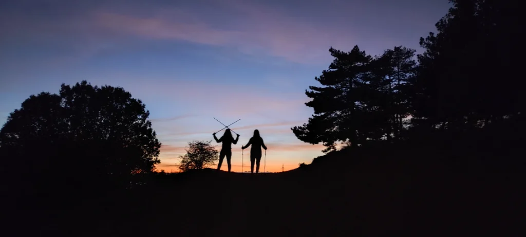 Mujeres practicando Marcha Nórdica en León al anochecer, con los bastones elevados mientras disfrutan del deporte al aire libre.